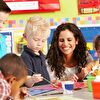 Children painting in kindergarten and the teacher smiling