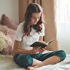 Teenager Girl Smiling While Reading on the Bed